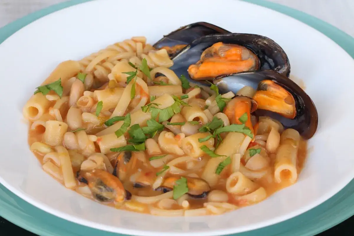 Un piatto invitante di pasta fagioli e cozze, con pasta corta, fagioli bianchi e cozze fresche, guarnito con prezzemolo.