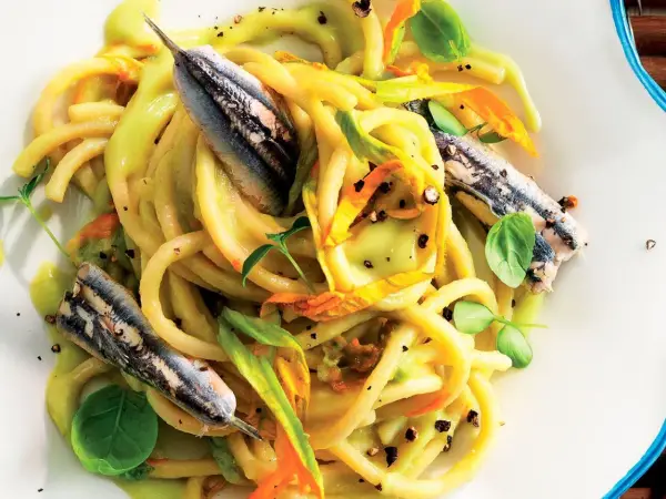 Pasta con fiori di zucca e alici, un piatto estivo colorato e saporito, con erbe fresche e pepe nero.