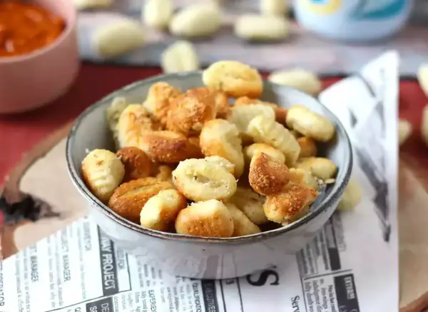 Gnocchi dorati e croccanti in friggitrice ad aria, serviti in una ciotola su carta di giornale.