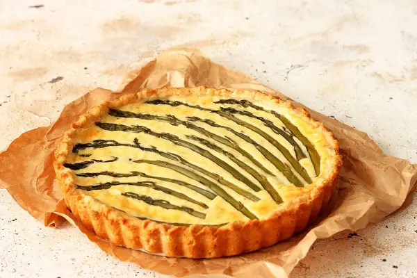 Torta salata asparagi con crosta dorata e ripieno cremoso, decorata con asparagi freschi disposti a raggiera.