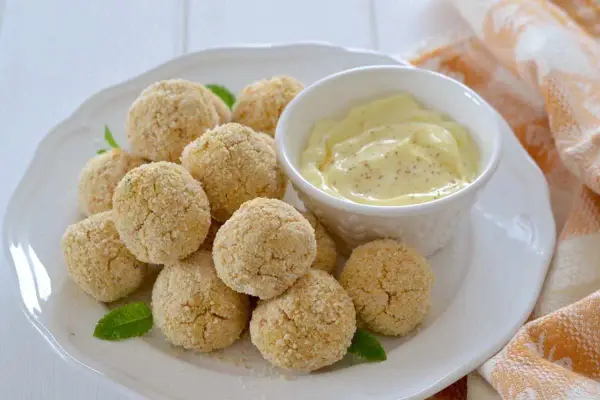 Polpette di ceci al forno dorate e croccanti, servite su un piatto bianco con una ciotolina di salsa cremosa e foglie di menta.