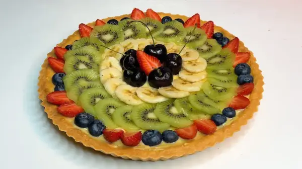 A fruit tart with kiwi, banana, strawberries, blueberries, and cherries on a custard filling.