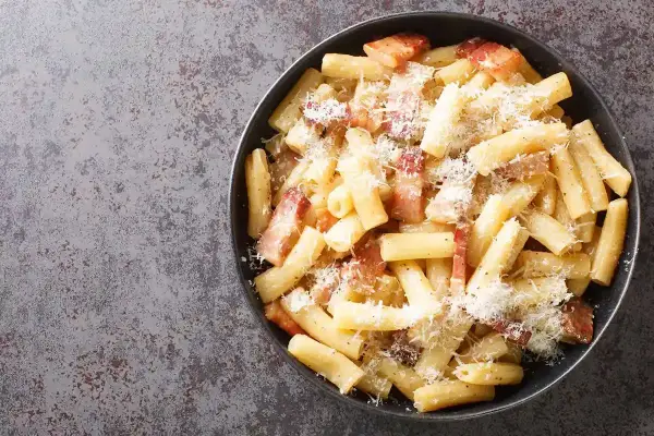 Un piatto di pasta alla zozzona fumante, con guanciale croccante e abbondante pecorino grattugiato, pronto per essere gustato.