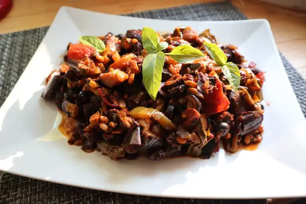 Un piatto di saporita caponata di melanzane, guarnita con foglie di basilico fresco.
