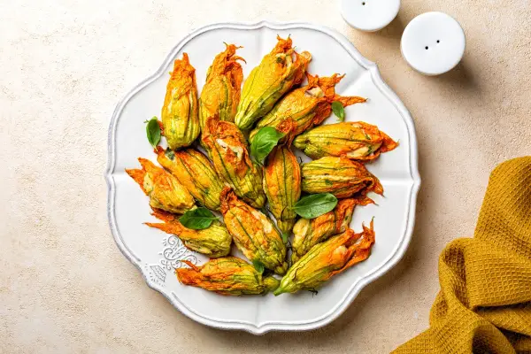 Fiori di zucca al forno ripieni, dorati e invitanti, disposti su un piatto bianco, con foglie di basilico fresco.