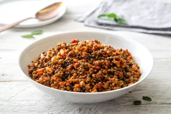 Un piatto invitante di lenticchie in umido, condite con pomodoro e cipolla, servite in una ciotola bianca su un tavolo di legno.