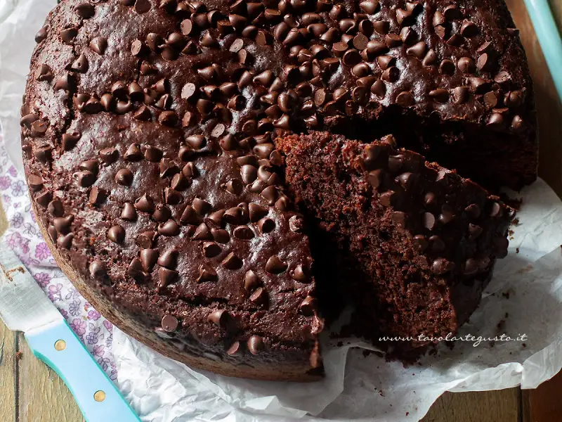 A rich, moist chocolate cake topped with chocolate chips, with a slice cut out to show its texture.