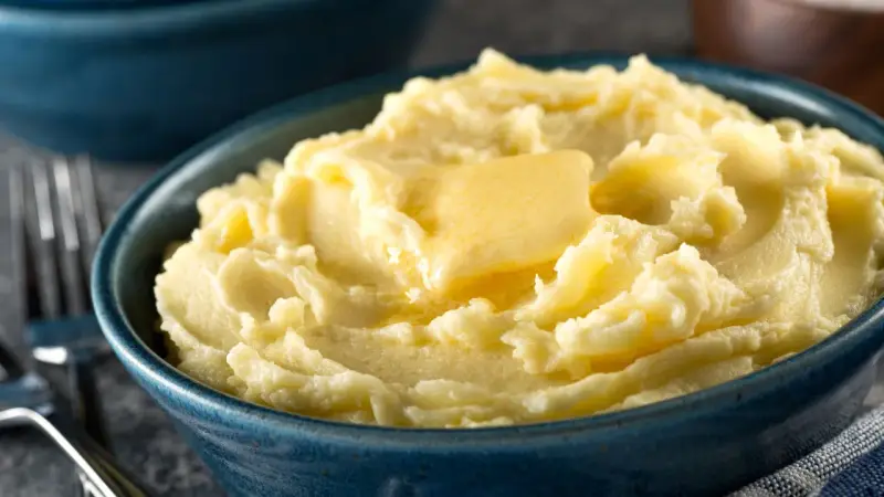 Una ciotola blu piena di soffice purea di patate, con una fetta di burro che si scioglie sopra.
